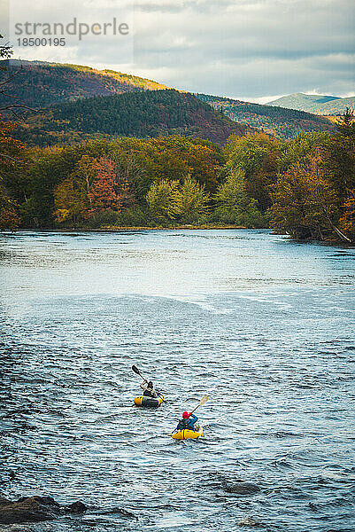 Zwei Paddler fahren mit Herbstlaub flussabwärts