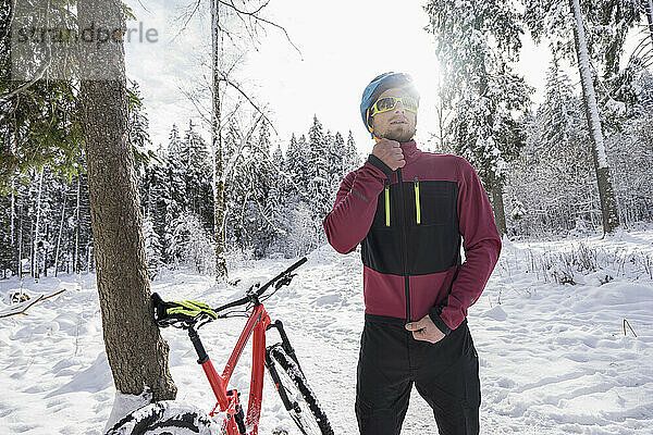 Junger Biker mit Reißverschlussjacke mit dem Fahrrad im Schnee