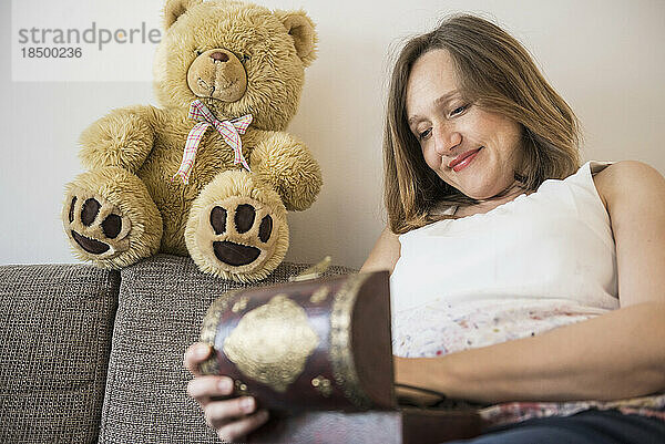 Glückliche schwangere Frau sitzt auf dem Sofa und schaut in die Schatztruhe  München  Bayern  Deutschland