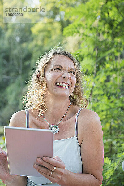 Schöne lächelnde Frau mit digitalem Tablet in der Natur  Deutschland