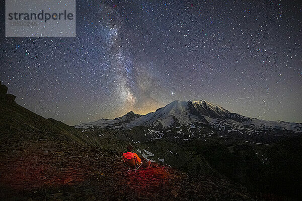Ein Mann sitzt und blickt auf die Milchstraße über dem Mt. Rainier
