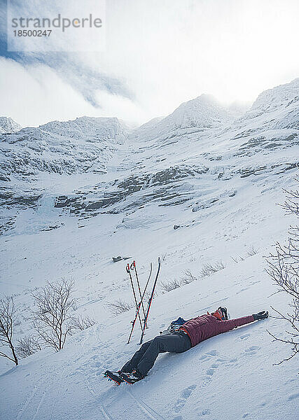 Mann liegt vor einem dramatisch verschneiten Bergrücken