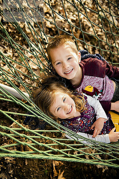 Lächelnder Bruder und Schwester entspannen sich im Herbst in der Hängematte und schauen in die Kamera