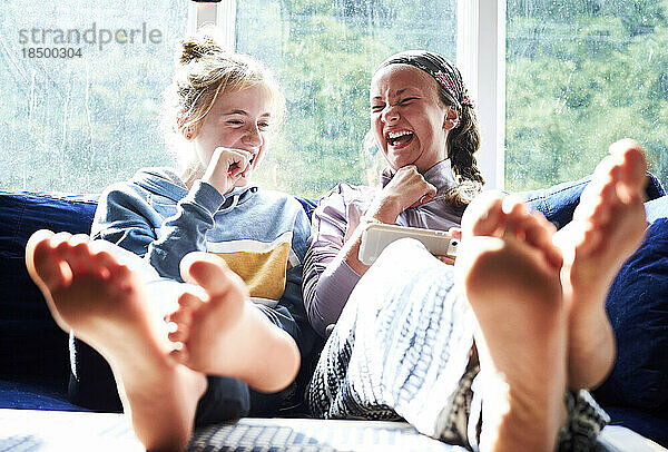 Junge Mädchen sitzen auf einer Couch  schauen auf einen Bildschirm und lachen