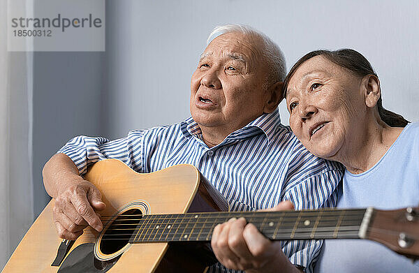 Älterer Mann spielt zu Hause Akustikgitarre und singt mit seiner Frau