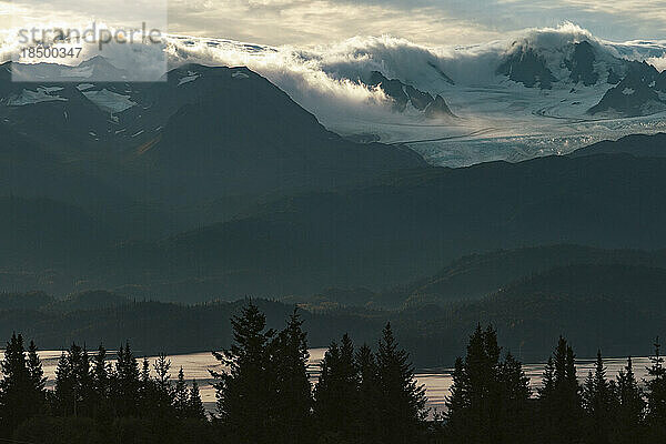 Vom Sonnenaufgang beleuchtete Morgenwolken rollen über einen Gletscher in Kachemak