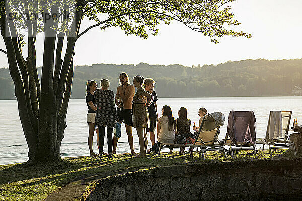 Gruppe junger Freunde feiert bei Sonnenuntergang am Seeufer  Bayern  Deutschland