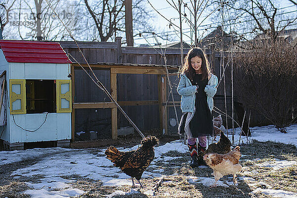 Ein glückliches kleines Mädchen steht im verschneiten Hof neben dem Hühnerstall