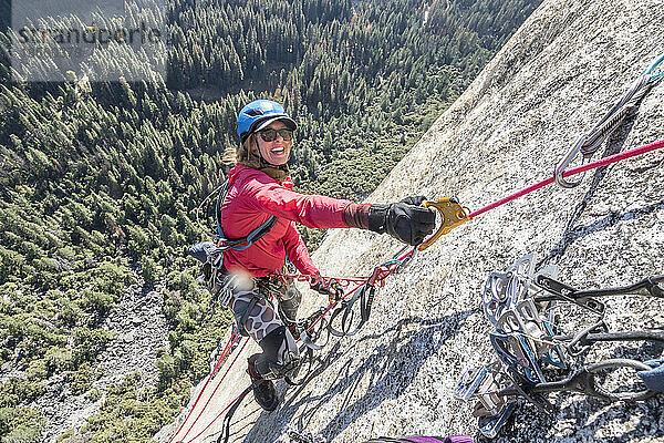 Eine junge Frau lächelt  während sie hoch oben auf einem Klettersteig klettert