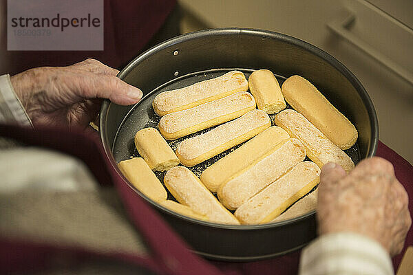 Ältere Frau hält eine mit Keksen gefüllte Kuchenform