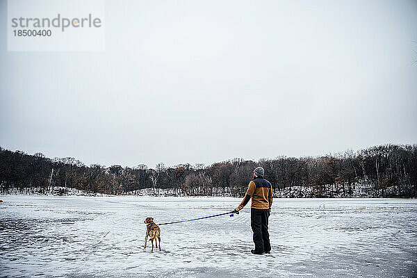 Brauner Hund und männlicher Besitzer erkunden gemeinsam einen zugefrorenen See