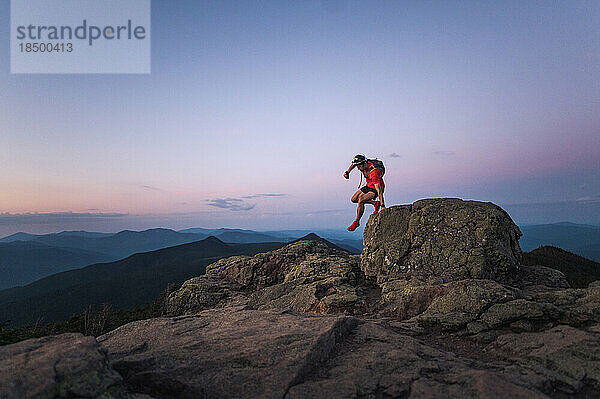 Trailrunner-Mann springt bei Sonnenaufgang vom Felsen auf dem Gipfel des Berges