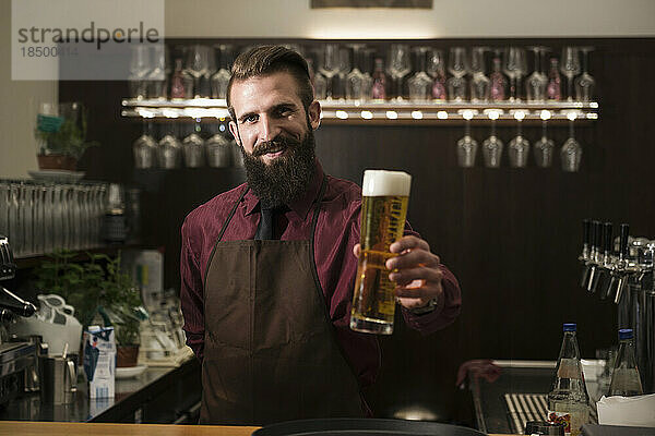 Porträt eines jungen Mannes  der ein Glas Bier anbietet