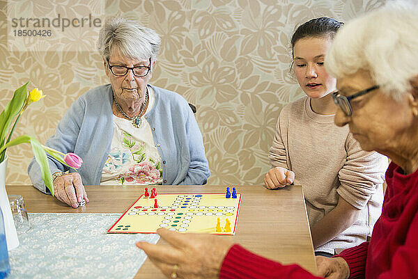 Mädchen spielt Brettspiel mit älteren Frauen im Altersheim