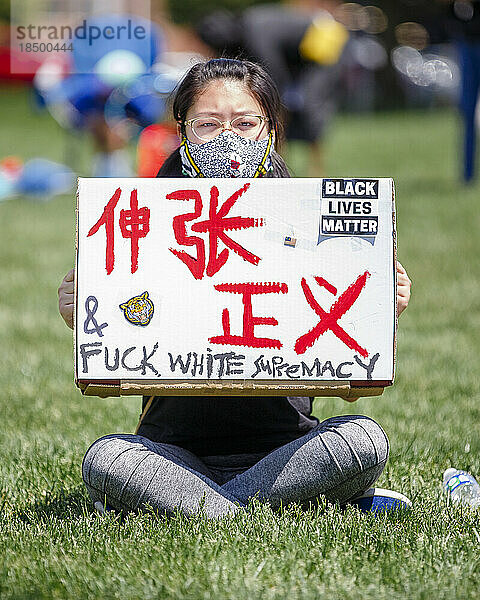 Eine junge Frau in Maske hält ein Protestschild gegen Rassismus