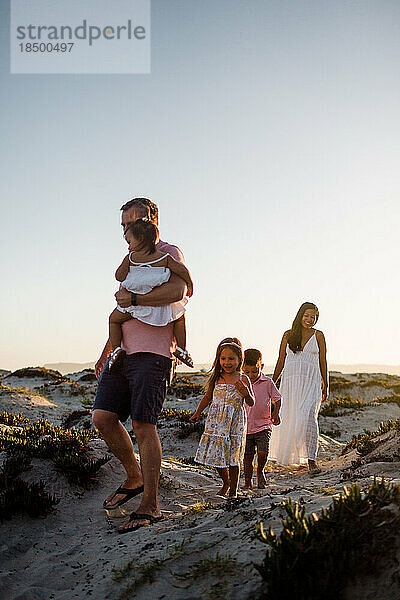 Fünfköpfige Familie spaziert bei Sonnenuntergang durch die Sanddünen am Strand von San Diego