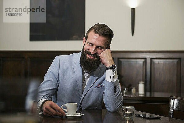 Gut gekleideter Mann schaut auf die Kaffeetasse und denkt nach  während er im Restaurant sitzt