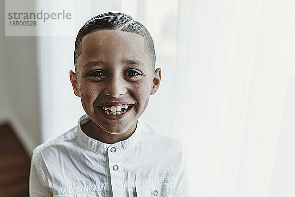Porträt eines kleinen Jungen  der im Studio mit natürlichem Licht in die Kamera lächelt