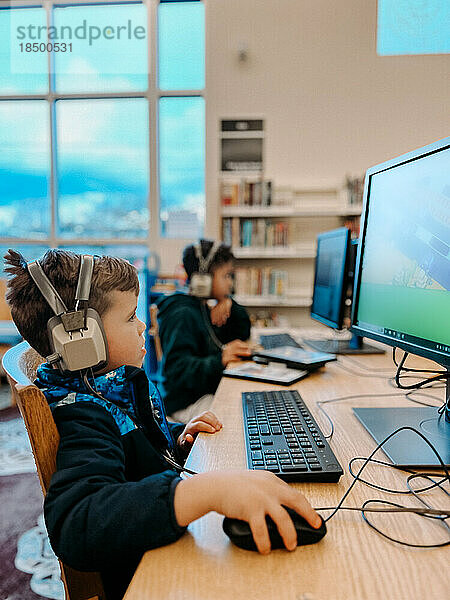 Grundschulbrüder spielen mit Kopfhörern am Computer in der Bibliothek