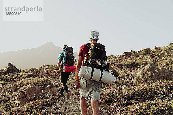 Zwei Männer gehen mit Campingausrüstung auf einem Wanderweg  im Hintergrund der Teide