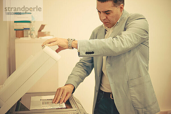 Junger erwachsener Mann benutzt einen Fotokopierer im Büro