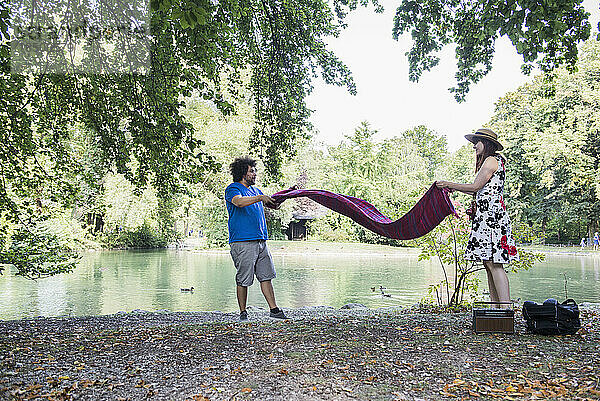 Paar breitet Decke für Picknick am Seeufer im Englischen Garten in München aus