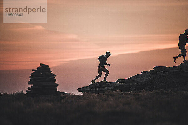 Silhouette männlicher Trailrunner  die bei Sonnenaufgang über den Bergrücken laufen