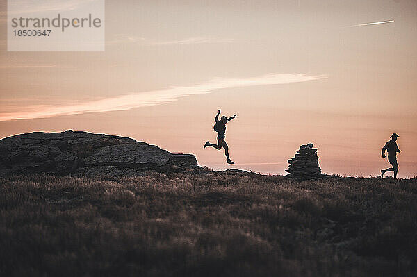 Silhouette männlicher Trailrunner  die bei Sonnenaufgang über den Bergrücken laufen