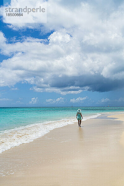 Rückansicht einer Frau  die am weißen Sandstrand in der Karibik spaziert.