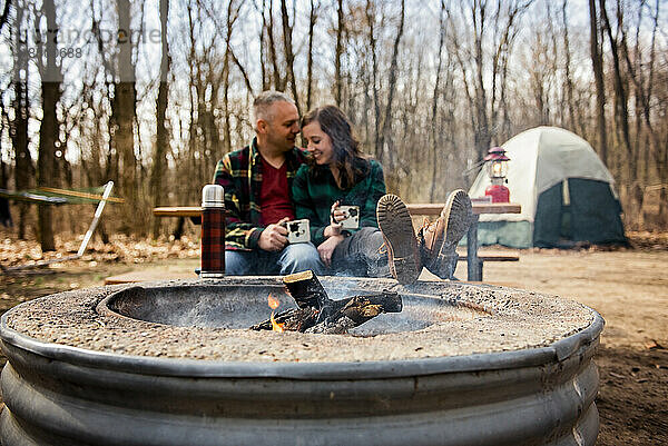 Lächelnder Mann und Frau trinken Kaffee und entspannen sich im Herbst am Lagerfeuer