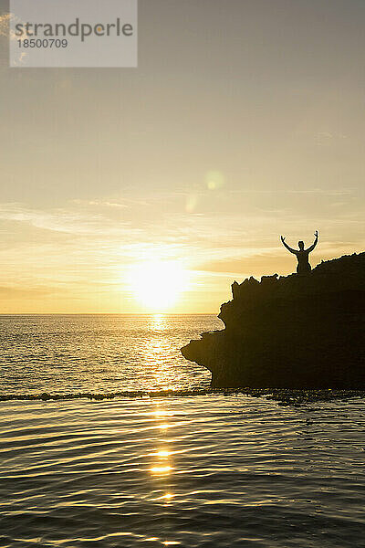 Silhouette eines Mannes  der bei Sonnenuntergang mit ausgestreckten Armen auf einer Klippe steht  Nusa Lembongan  Bali  Indonesien