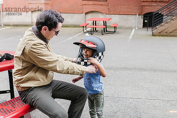 Lächelnder Mann hilft Kleinkind  draußen Motorradhelm aufzusetzen