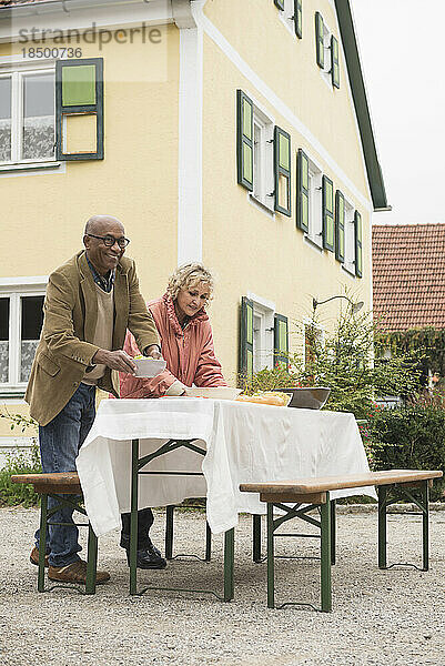 Älteres erwachsenes Paar bereitet einen Picknicktisch draußen im Bauernhaus vor  Bayern  Deutschland