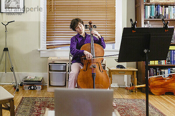 Ein junger leidenschaftlicher Junge spielt Cello vor dem Computer