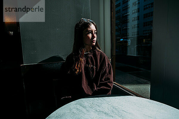 Ruhiges Teenager-Mädchen sitzt im Café und schaut aus dem Fenster