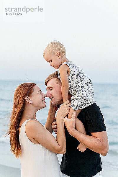 Seitenansicht einer glücklichen Familie mit einem kleinen Kind  das sich am Strand umarmt