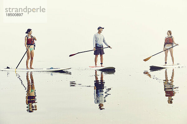 Eine Gruppe von Freunden beim Standup-Paddle-Boarding an einem frühen nebligen Morgen