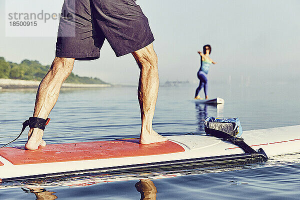 Ein Standup-Paddle-Boarder balanciert bei Sonnenaufgang im Nebel in einer Yoga-Pose