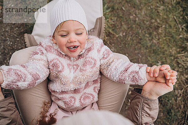 Zahnloses kleines Mädchen in den Armen ihrer Mutter draußen bei kaltem Wetter