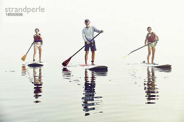 Eine Gruppe von Freunden beim Standup-Paddle-Boarding an einem frühen nebligen Morgen