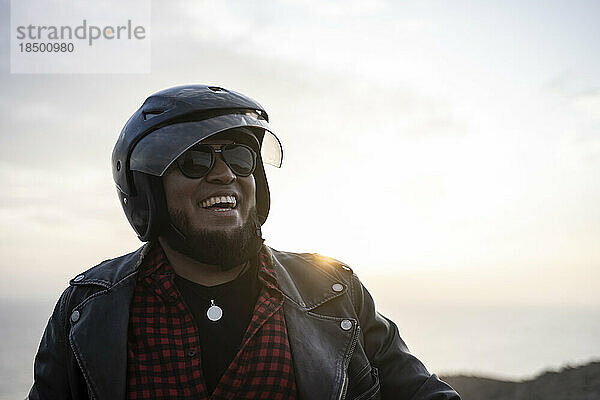 Bärtiger Biker lächelt bei Sonnenuntergang.