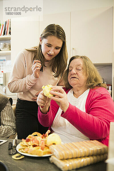 Ältere Frau mit Mädchen schneidet Apfel im Pflegeheim