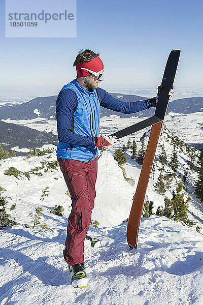 Mann hält Skier am Berg