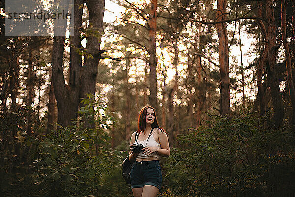 Junge Frau hält Kamera beim Spaziergang im Wald