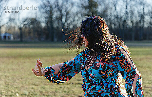 Seitenansicht einer Frau  die draußen mit vom Wind verwehten Haaren tanzt