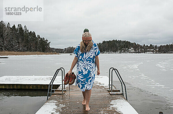 Frau geht auf einem Steg und ist bereit  im kalten Wasser schwimmen zu gehen