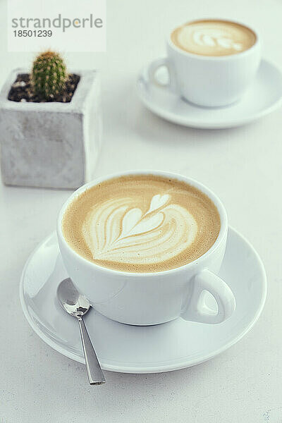 Heiße Latte Macchiato in weißen Kaffeebechern auf einem Marmortisch mit Kaktus.