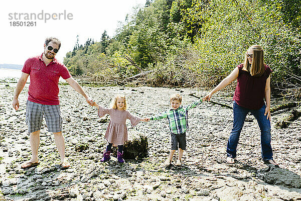 Familienporträt von Eltern und Kindern  die sich an einem Strand an den Händen halten