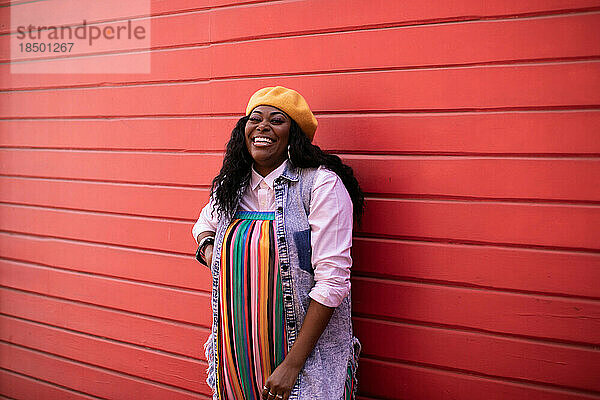 Schwarze erwachsene Frau lacht in Richtung Kamera mit roter Wand