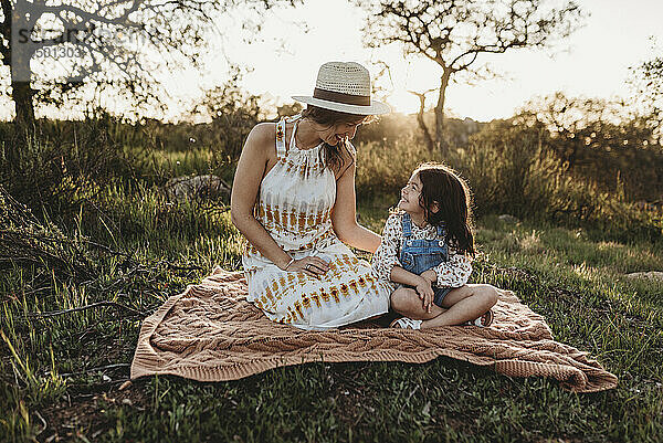 Mutter und kleine Tochter sitzen auf einer Decke auf einer Wiese im Gegenlicht
